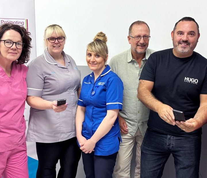 Päť usmievavých ľudí stojí spolu v zdravotníckom oblečení, pričom dvaja z nich držia prekladač.